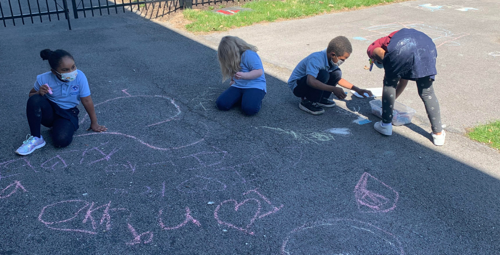 Students express their creativity with sidewalk chalk during their outdoor recess.